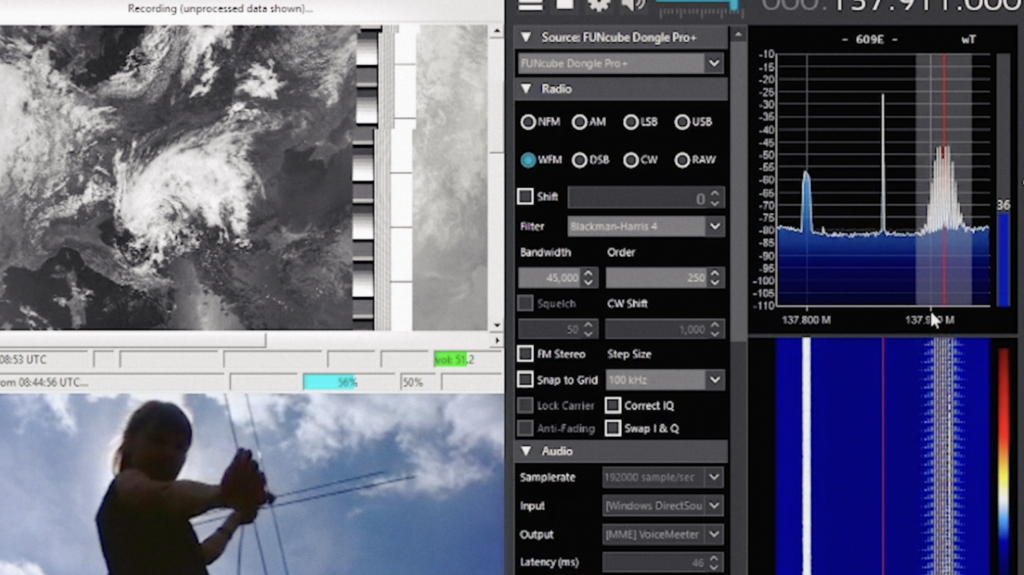 Software on a laptop decodes the data from her antenna. One window shows satellite images of cloud movement and another tracks her own movements through the webcam. On the right, radio signals spike up and down on a graph.