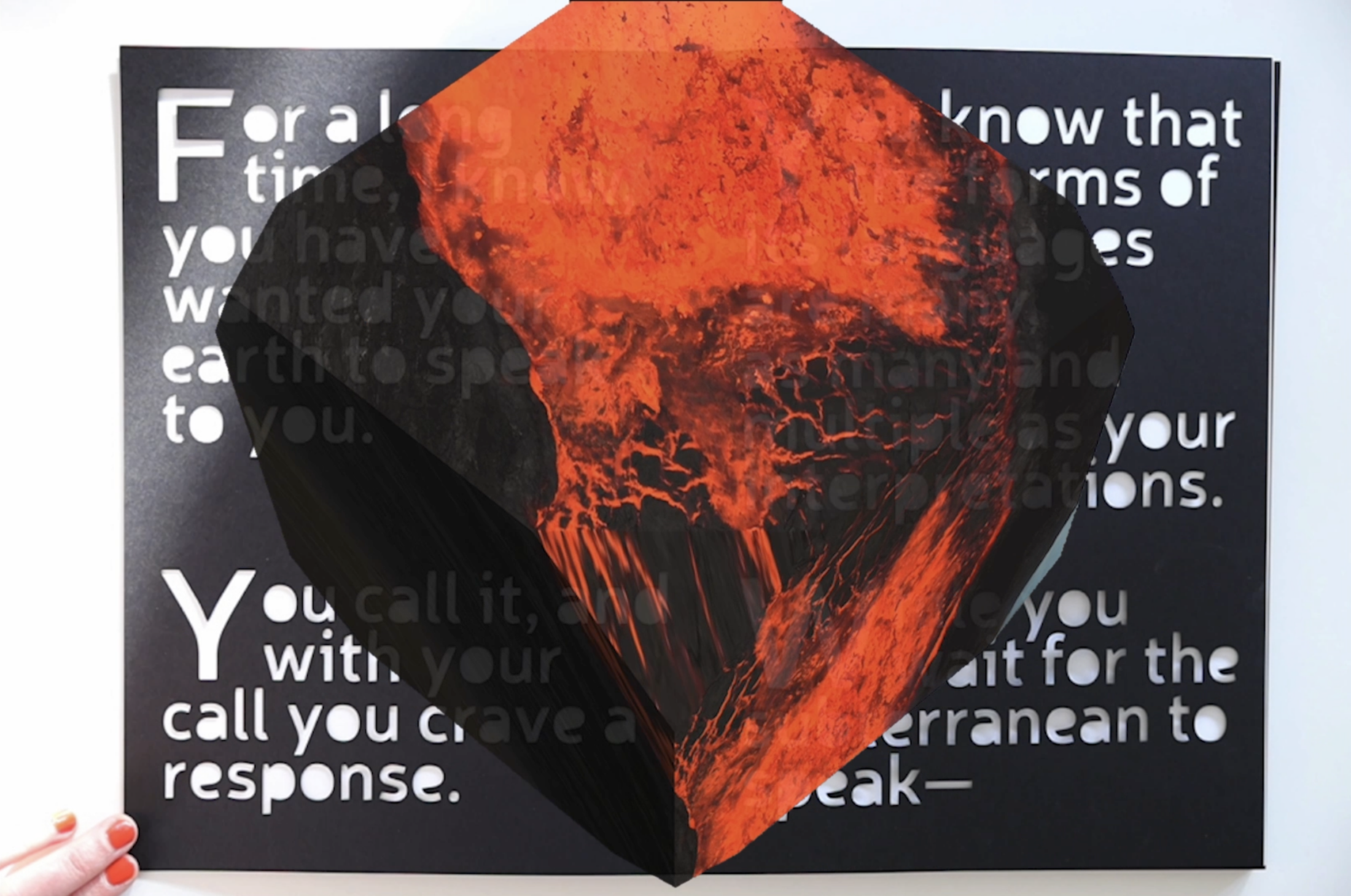 A hand opens a book with large type. A simulated hologram of a stone appears in the center.